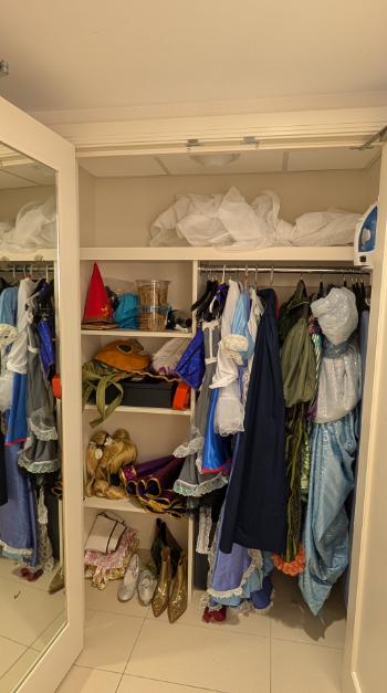 A photo of a hotel room closet, stuffed with many cosplay outfits on hangers, with other costume pieces on the shelves. The closet is very full of clothing in many colors and textures.